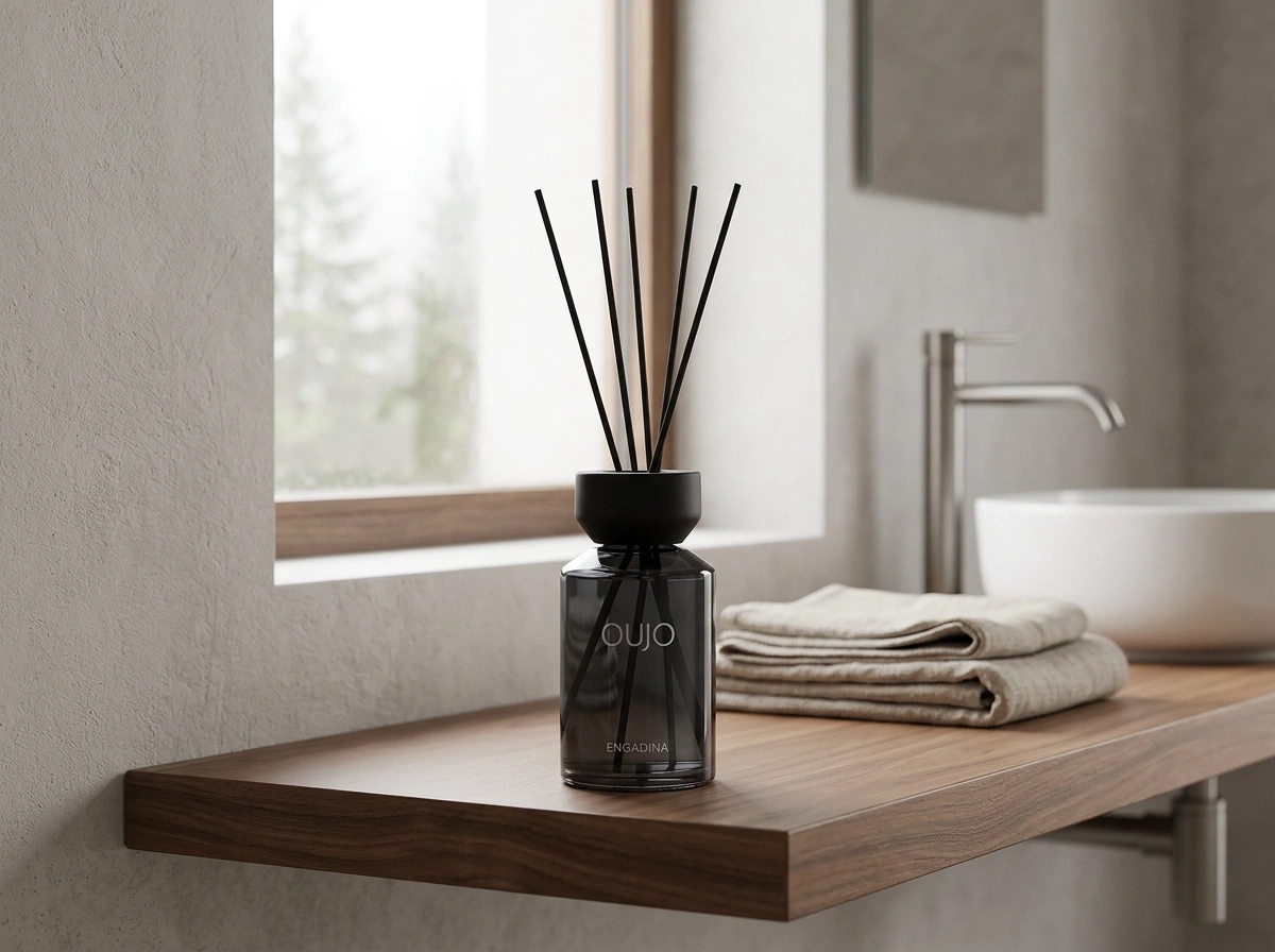 A diffuser with sticks on a wooden shelf in a bathroom next to folded towels and a sink.