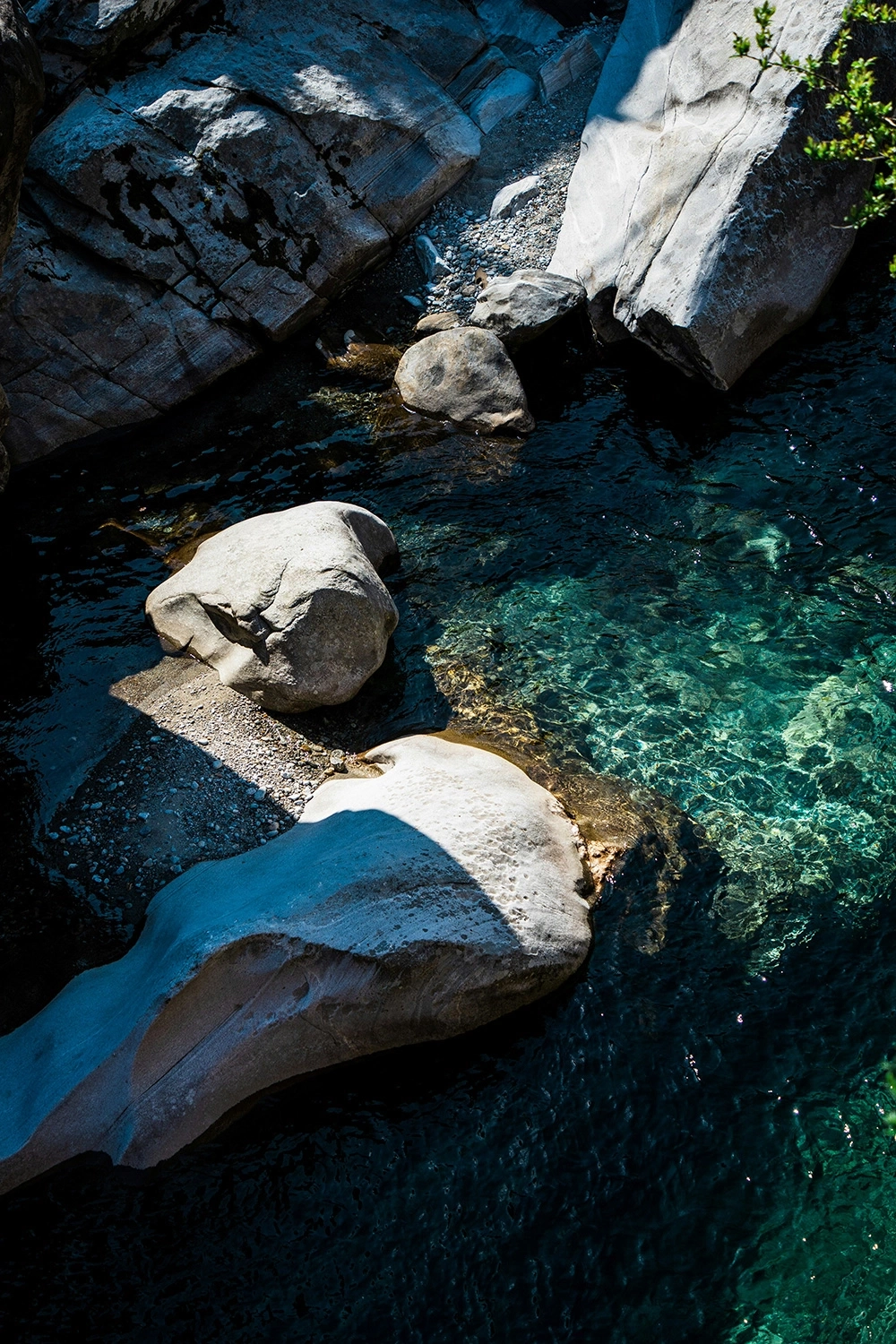 A stream flows over smooth rocks in shade and sunlight.