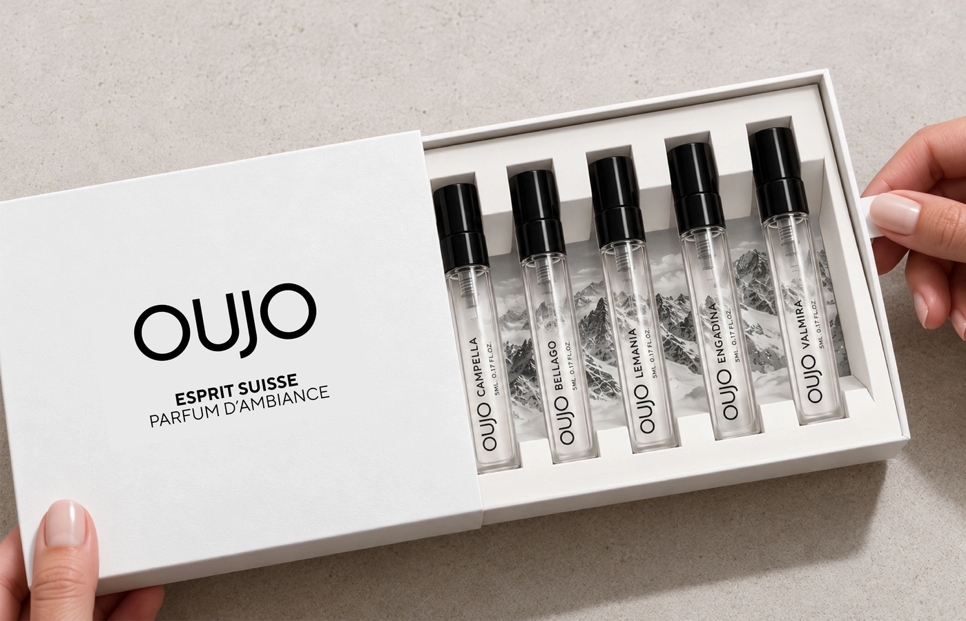 A set of OUJO perfume samples in a white box with mountain scenery in the background.