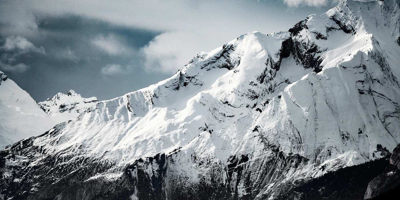 Snow-covered mountain range under a dramatic sky with clouds.