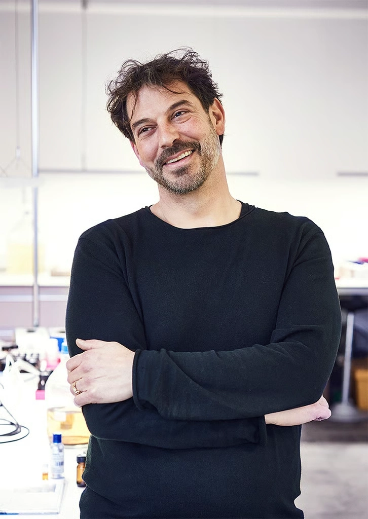 A man with dark hair and beard smiles at the camera, his arms crossed.